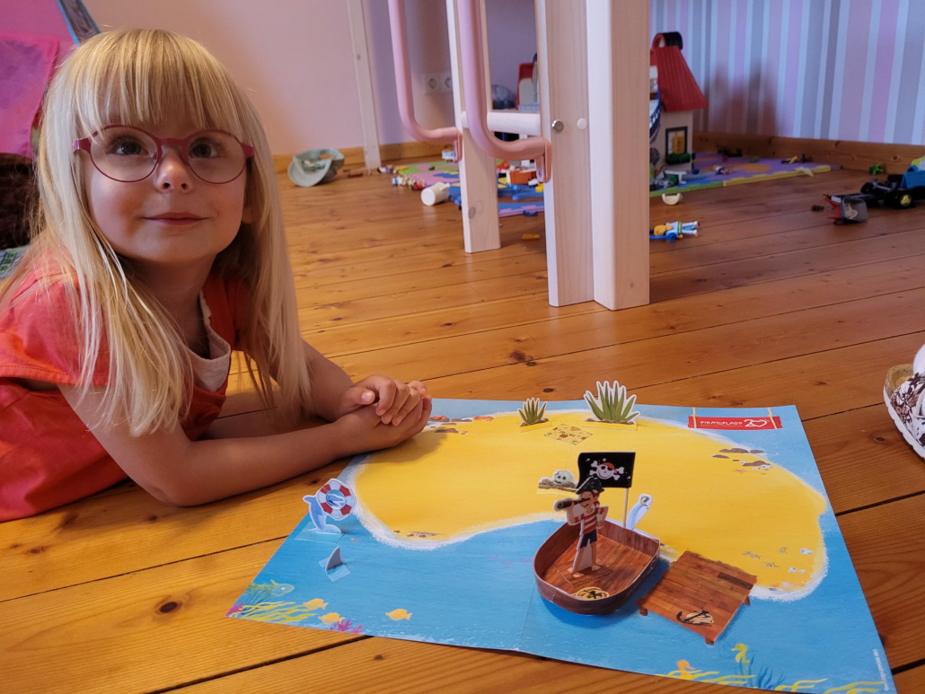 Mädchen im Kinderzimmer liegt glücklich neben der gebastelten Piratoplast Pirateninsel