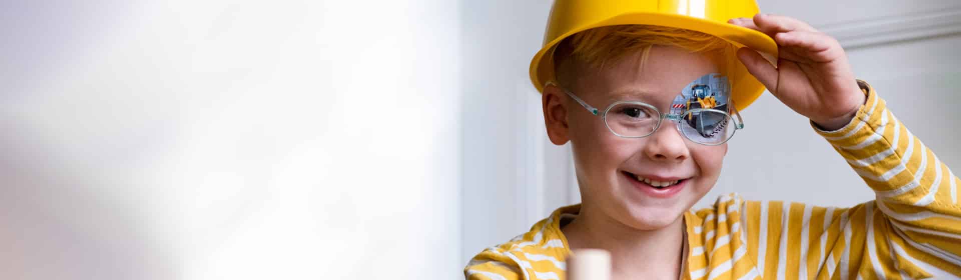 Junge mit Bauarbeiterhelm und Augenpflaster Motiv Bagger lächelt in die Kamera